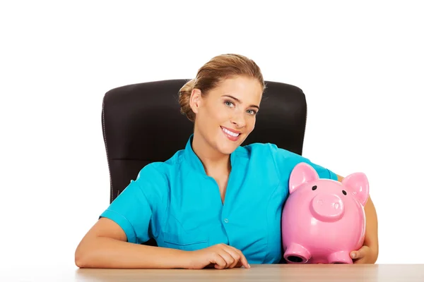 Young female doctor or nurse holding piggybank — Stock Photo, Image