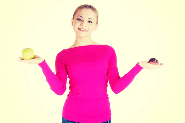 Mujer casual joven sosteniendo una manzana y una galleta . — Foto de Stock