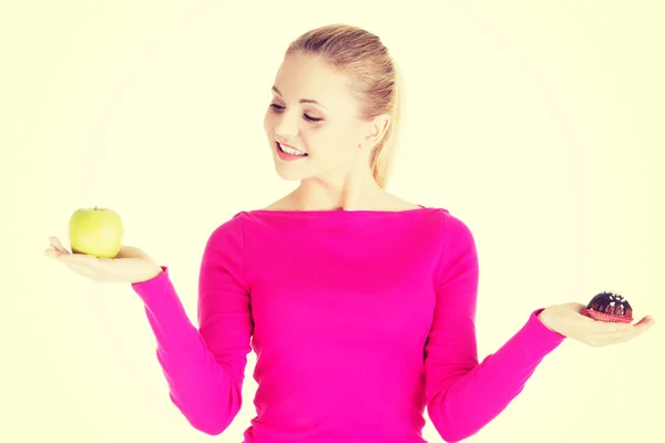 Mujer casual joven sosteniendo una manzana y una galleta . — Foto de Stock