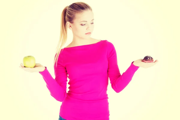 Mujer casual joven sosteniendo una manzana y una galleta . — Foto de Stock
