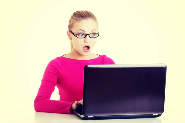 Jonge vrouw achter laptop zit verrast. — Stockfoto