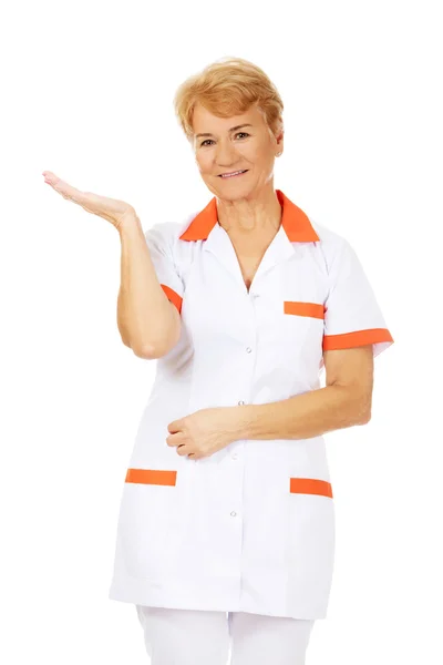 Sorridi anziana dottoressa o infermiera che preannuncia qualcosa a palmo aperto — Foto Stock