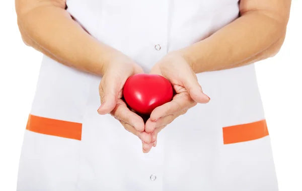 Podeszłym wieku kobieta lekarz lub pielęgniarka trzymając czerwony zabawka serca — Zdjęcie stockowe