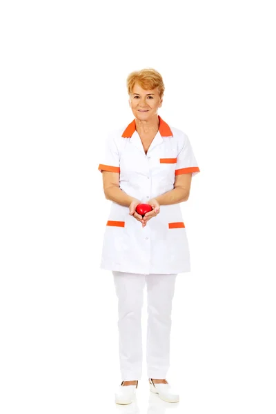 Smile elderly doctor or nurse holding red toy heart — Stock Photo, Image