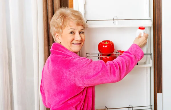Старша жінка бере пляшку молока з холодильника — стокове фото