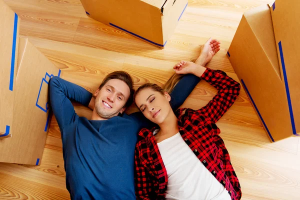 Casal feliz deitado no chão em nova casa com caixas de papelão ao redor Imagem De Stock