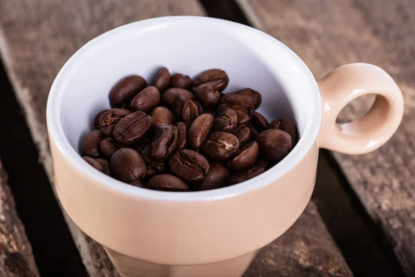 Graine de café en tasse beige sur planche de bois — Photo