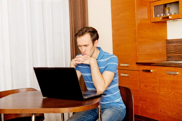 Молодой человек сидит за столом и пользуется ноутбуком — стоковое фото