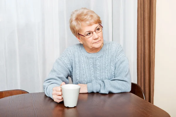 Старша жінка сидить за столом і п'є каву або чай — стокове фото