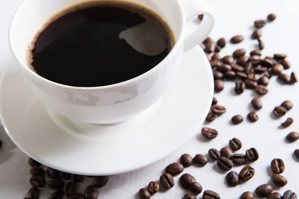 Weiße Tasse mit Kaffee und Kaffeesamen auf dem Tisch — Stockfoto