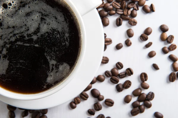 Tasse blanche avec café et graines de café sur la table — Photo