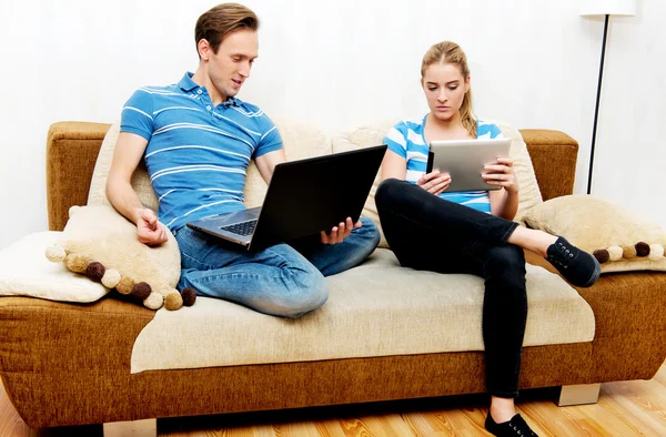 Casal jovem relaxante no sofá e usando tablet e laptop — Fotografia de Stock