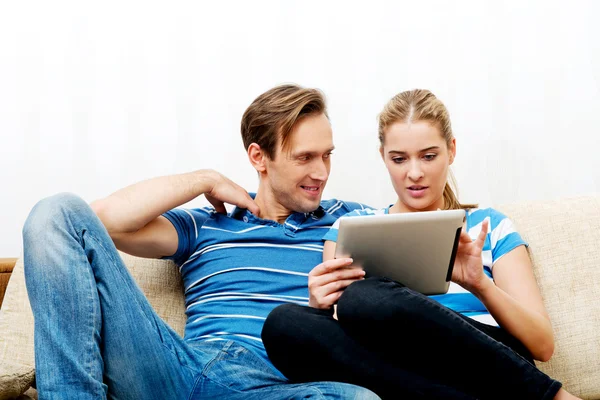 Casal jovem sentado em casa e à procura de algo no tablet — Fotografia de Stock