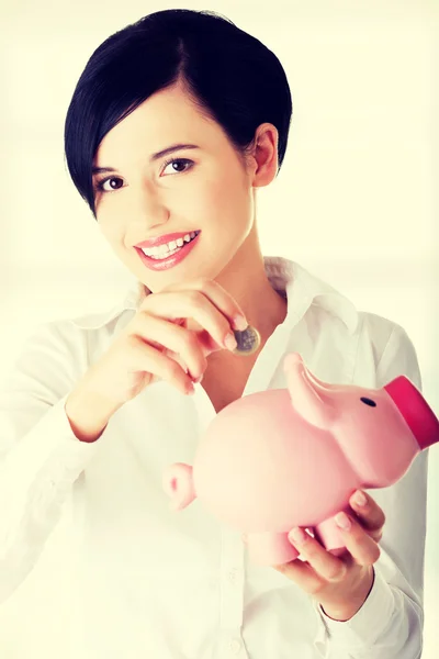 Empresária colocando uma moeda em um banco porquinho — Fotografia de Stock