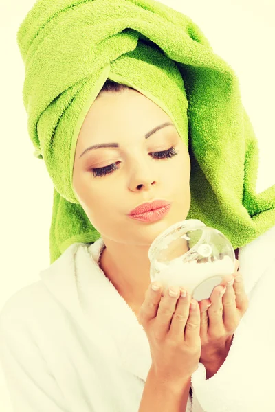 Mulher bonita em roupão de banho, turbante e segurando creme facial . — Fotografia de Stock
