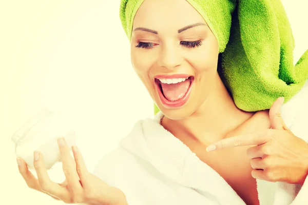 Mooie vrouw in badjas, tulband en bedrijf gezichtscrème. — Stockfoto