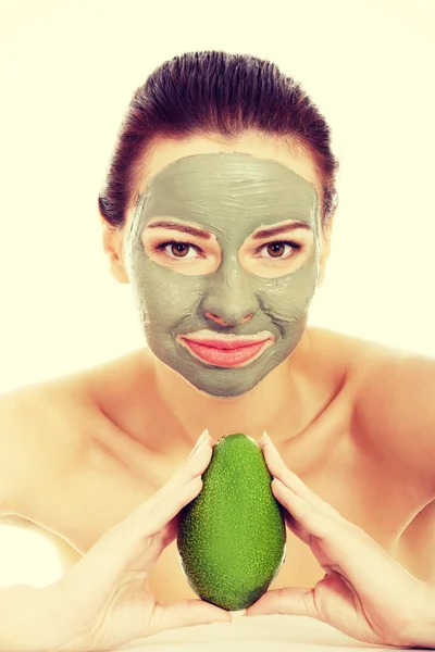 Beautiful woman with facial mask holding avocado. — Stock Photo, Image