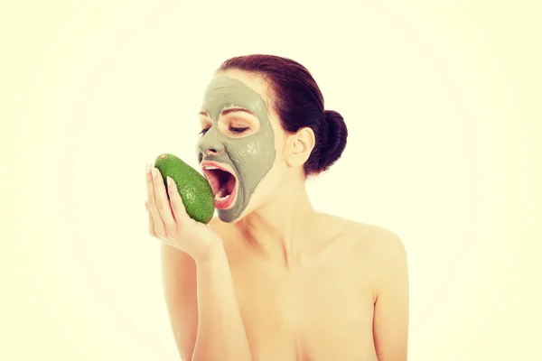 Hermosa mujer con máscara facial sosteniendo aguacate . — Foto de Stock