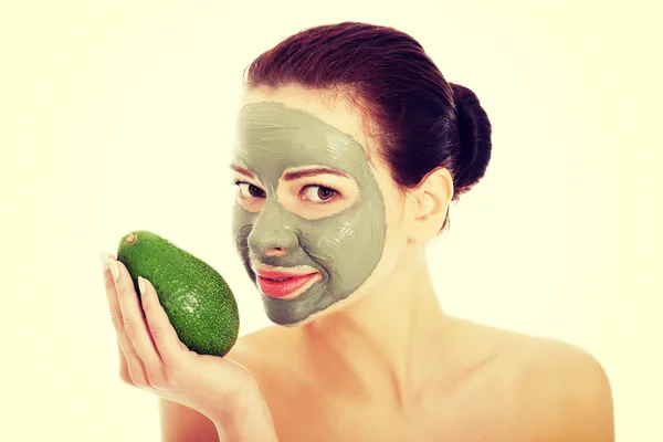 Hermosa mujer con máscara facial sosteniendo aguacate . — Foto de Stock