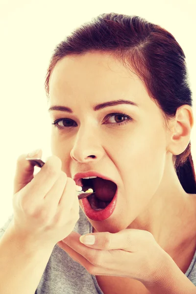 Jovem mulher casual comendo pílulas em uma colher . — Fotografia de Stock