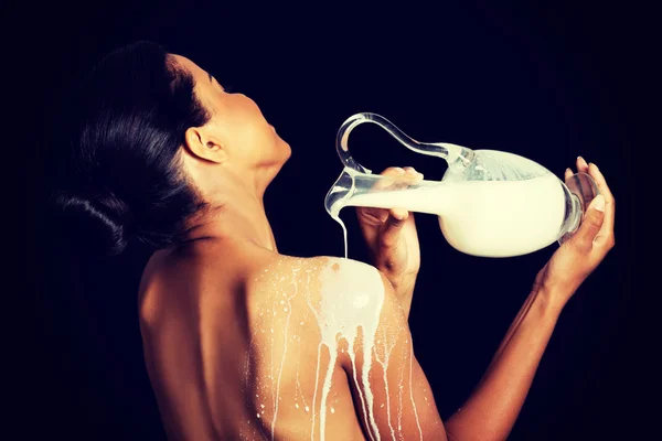 Schöne nackte Frau gießt Milch auf ihren Rücken. — Stockfoto
