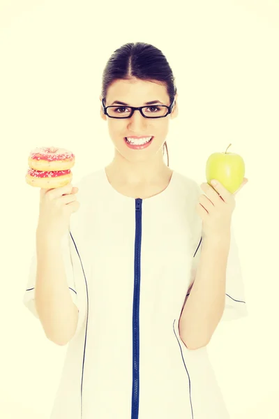 Junge Ärztin, Krankenschwester mit einem Apfel und Donuts. — Stockfoto