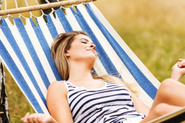 Genç sarışın kadın hamakta dinleniyor.