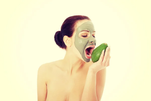 Mooie vrouw met gezichts masker houden avocado. — Stockfoto