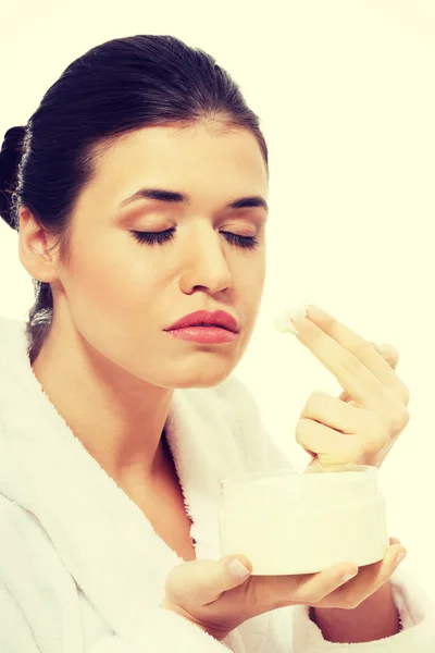 Mooie vrouw in badjas met gezichtscrème. — Stockfoto