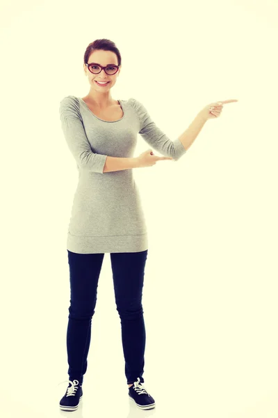 Beautiful casual woman in eyeglasses pointing aside. — Stock Photo, Image