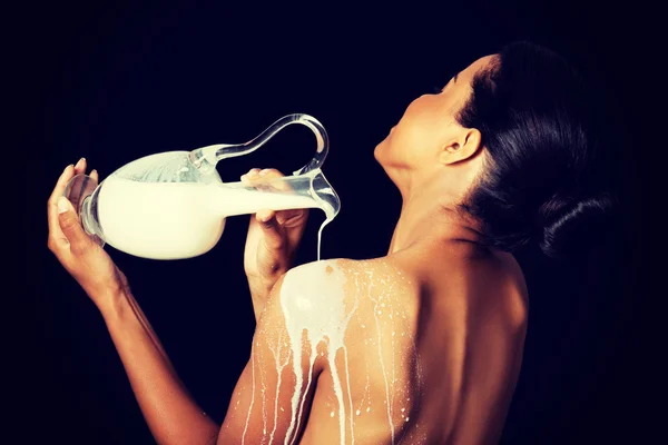 Mulher nua bonita está derramando leite em suas costas . — Fotografia de Stock