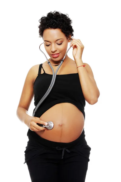 Беременная женщина со стетоскопом слушает ребенка — стоковое фото
