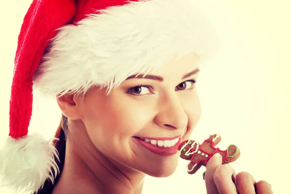 Schöne Frau mit Weihnachtsmannhut isst einen Keks. — Stockfoto