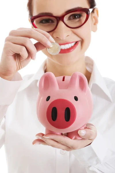 Vrouw in brillen geld om spaarpot — Stockfoto