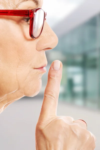 Äldre kvinna har finger på läpparna. — Stockfoto