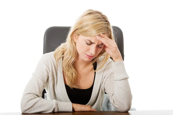 Tired woman sitting at the desk touching head — Stock Photo, Image