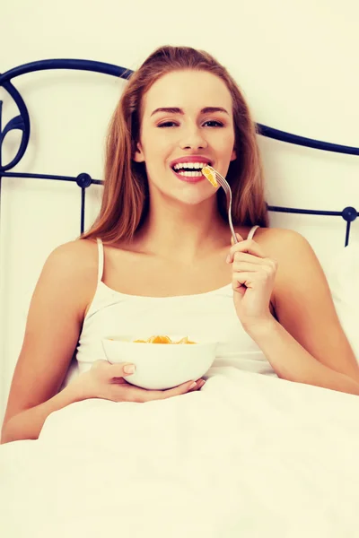 Schöne kaukasische Frau isst frisches Obst im Bett. — Stockfoto