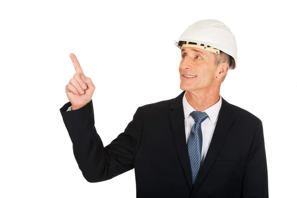 Hombre de negocios sonriente con el sombrero duro apuntando hacia arriba —  Fotos de Stock