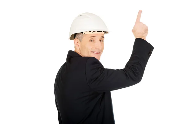 Hombre de negocios sonriente con el sombrero duro apuntando hacia arriba —  Fotos de Stock