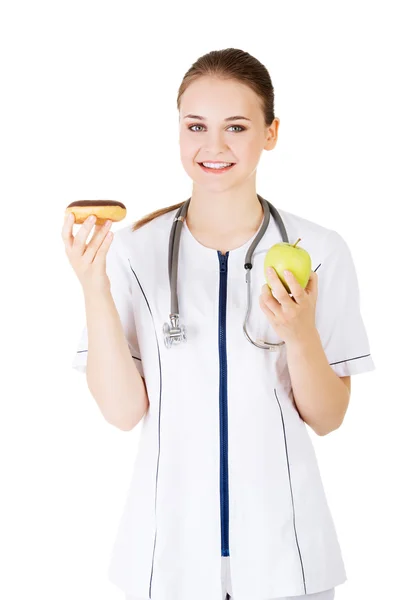 Женщина-врач держит яблоко и пончик — стоковое фото