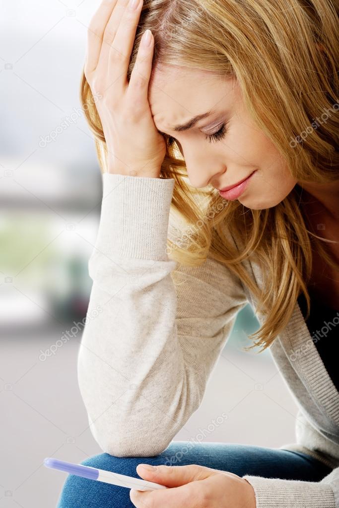 Sad young woman holding pregnancy test