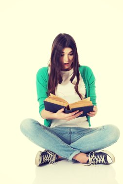 Genç bir kadın oturuyor ve kitap okuyor..
