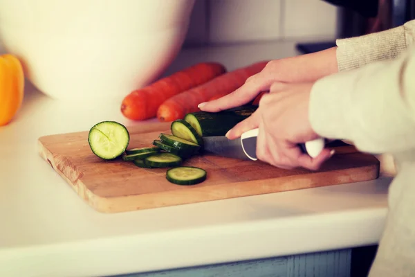 Woman cutting cucumber on kitchen board. — Stock Photo, Image