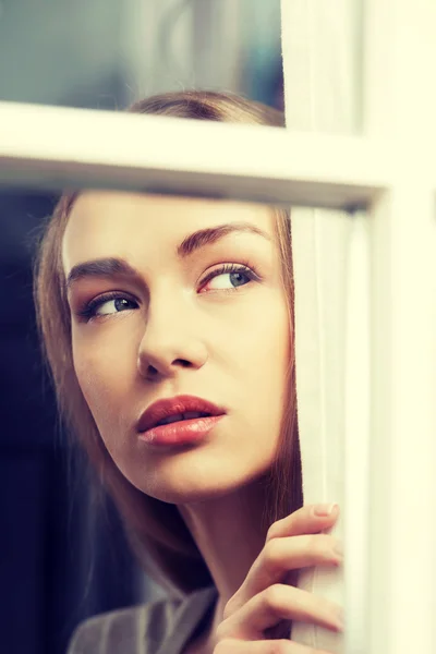 Beautiful woman is looking through window. — Stock Photo, Image