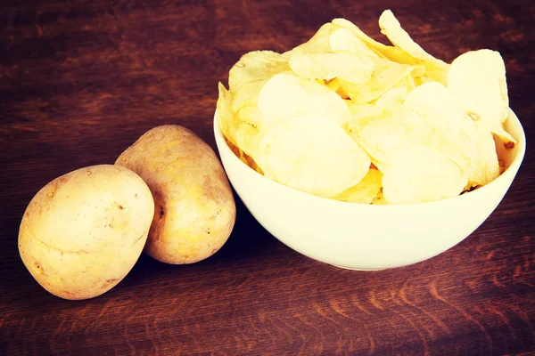 Potatoe chips in a bowl and potatoes. — Stock Photo, Image