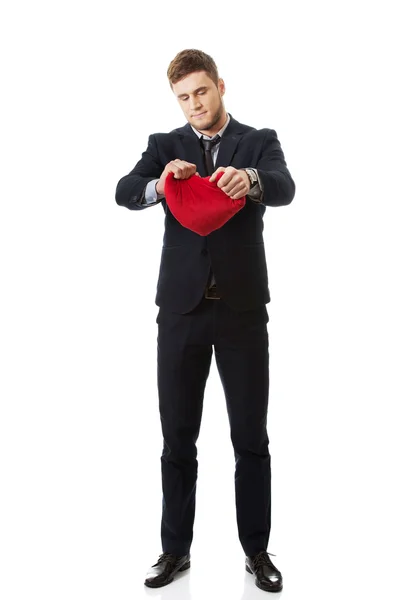 Businessman tears heart shaped pillow. — Stock Photo, Image