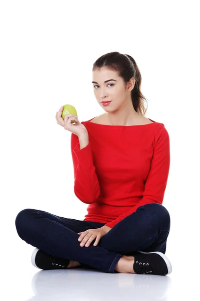 Женщина сидит со скрещенными ногами, держа яблоко — стоковое фото