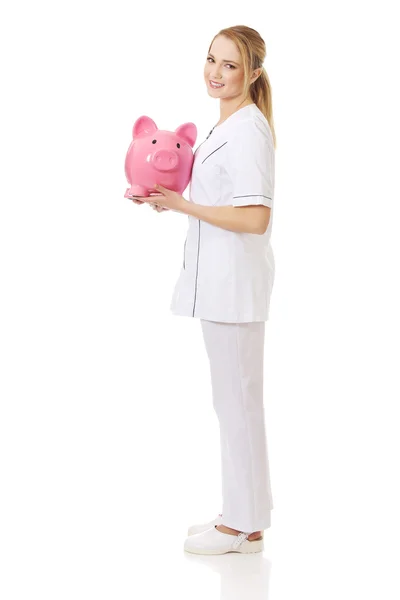 Ung kvinnlig läkare innehar en piggybank. — Stockfoto