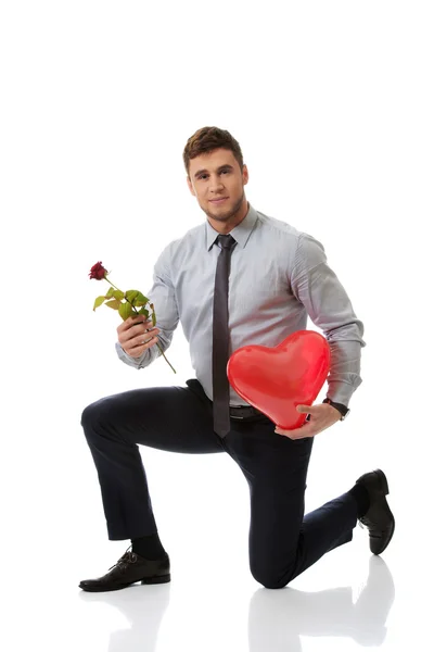 Hombre arrodillado con rosa roja y globo del corazón . — Foto de Stock