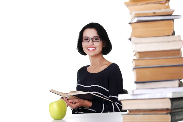 Glückliche Frau sitzt an einem Schreibtisch mit einem Stapel Bücher — Stockfoto